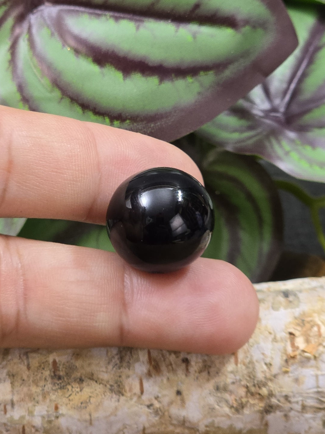 Schwarze runde Edelsteinperle zur Größendarstellung zwischen den Fingern