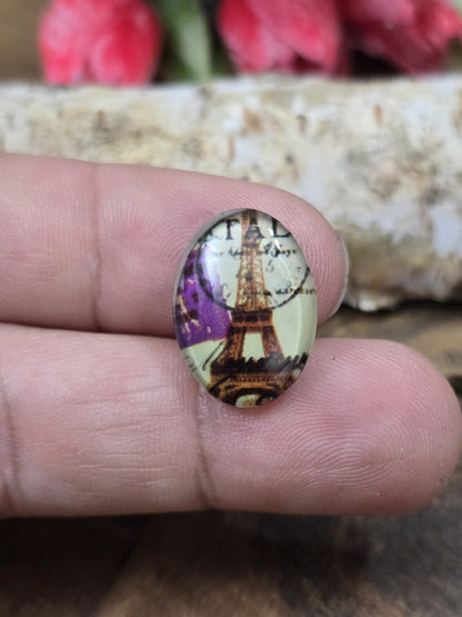Ein ovaler Vintage-Glascabochon (18x13 mm) mit Eiffelturm und Motiv-Details in Paris-Optik auf einer Fingerspitze als praktischer Größenvergleich für DIY-Schmuck.