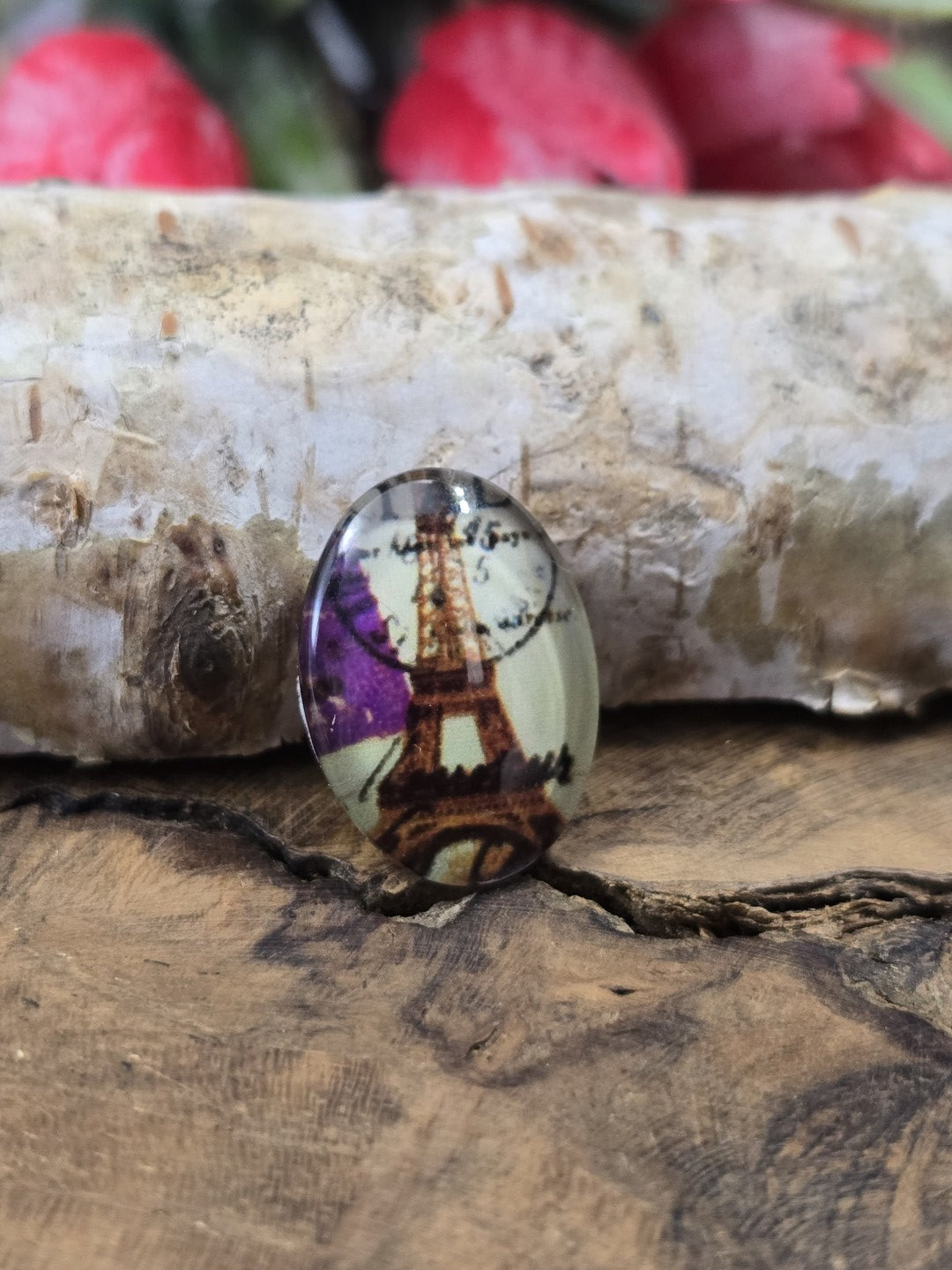Nahaufnahme eines einzelnen ovalen 18x13 mm Cabochons aus Glas mit französischem Eiffelturm-Motiv und violetten Blüten als Zubehör zum Basteln von Medaillons, Ringen oder Ketten.