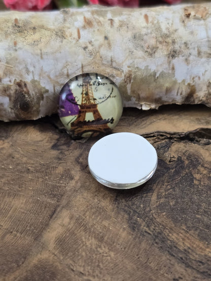 Zwei runde Paris-Glascabochons auf Holz, bei denen einer mit der flachen, weißen Rückseite nach oben liegt, um die Klebefläche für Fassungen zu zeigen.