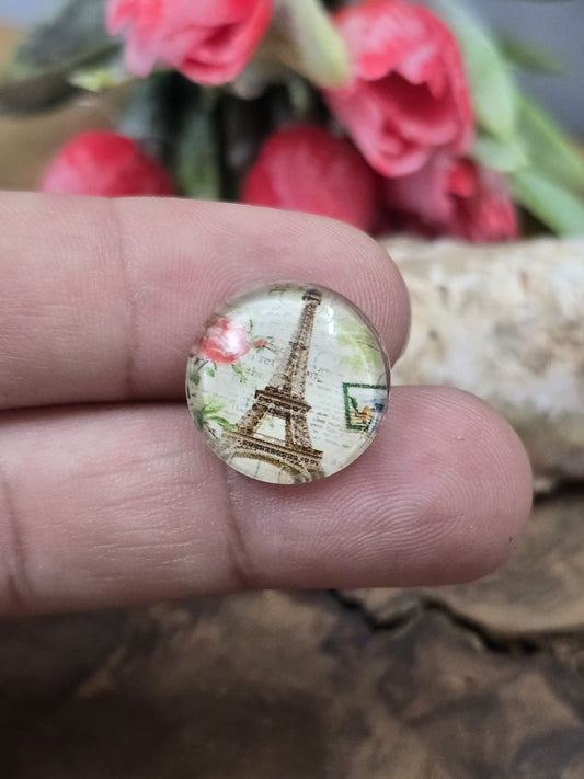 Ein kleiner runder Eiffelturm-Glascabochon (16 mm) im romantischen Vintage-Stil auf einer Fingerkuppe präsentiert zum Größenvergleich.