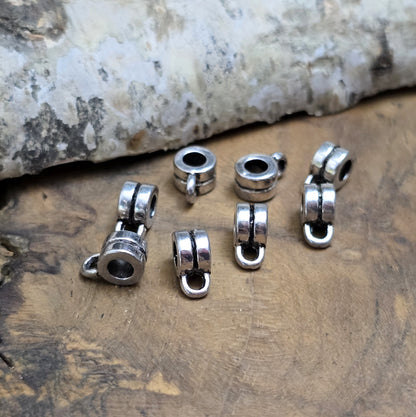 Das Bild zeigt antiksilberfarbene Metallperlen mit Öse. Sie sind eine ideale Ergänzung für kreative Schmuckprojekte. Dank des großzügigen 3-mm-Lochs lassen sie sich mühelos auf verschiedene Bänder und Kordeln auffädeln. Die zusätzliche Öse eröffnet zahlreiche Designmöglichkeiten, um Schmuckstücke individuell zu gestalten.