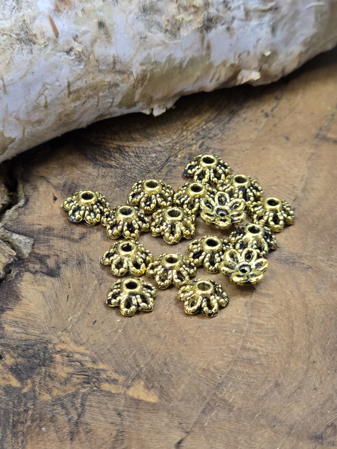 Mehrere kleine Metall Perlenkappen in Antikgold auf Holzuntergrund fotografiert