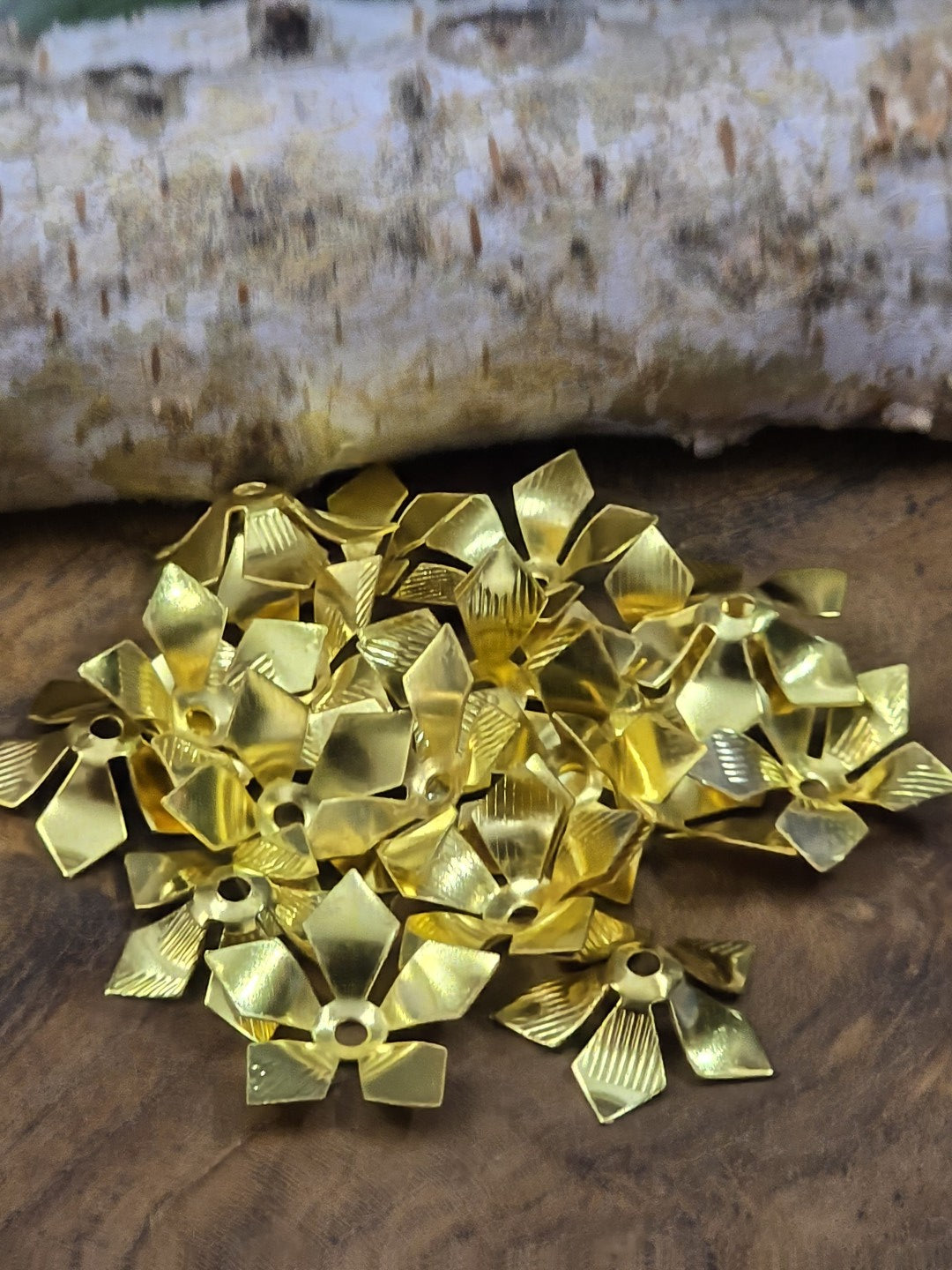 Goldfarbene Perlenkappen in Blütenform 16 mm auf Holzgrund vor Birkenholz