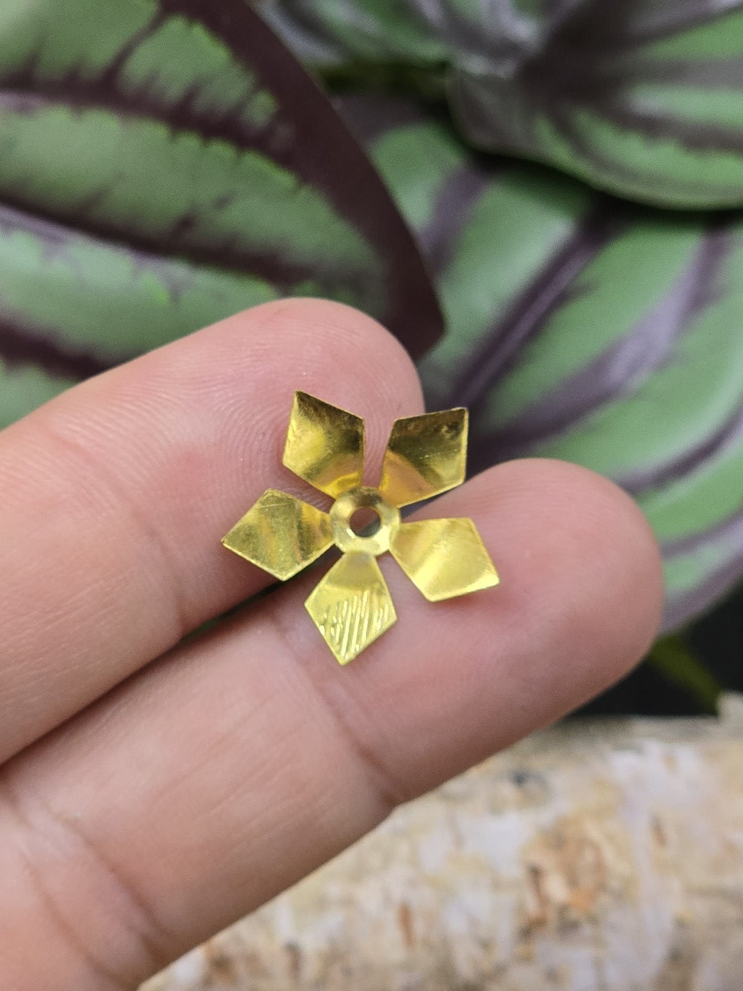 Fünfblättrige goldene Perlenkappe 16 mm als Größenvergleich auf der Fingerspitze