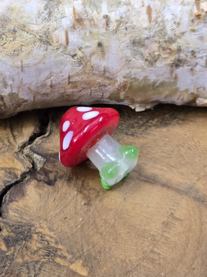 Seitlich fotografierte Fliegenpilz-Glasperle in Rot, Weiß und Grün auf Holzuntergrund