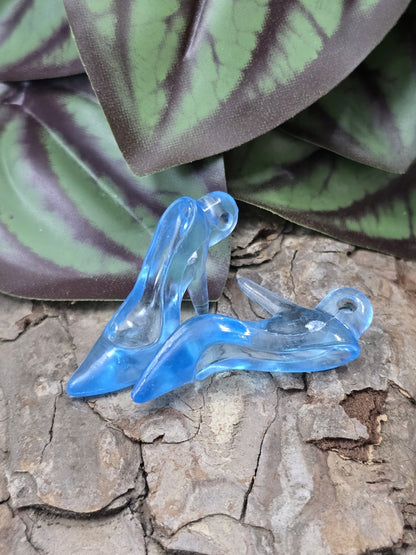 Zwei transparente hellblaue Acryl-Pumps als High-Heel-Schmuckanhänger auf Holzgrund