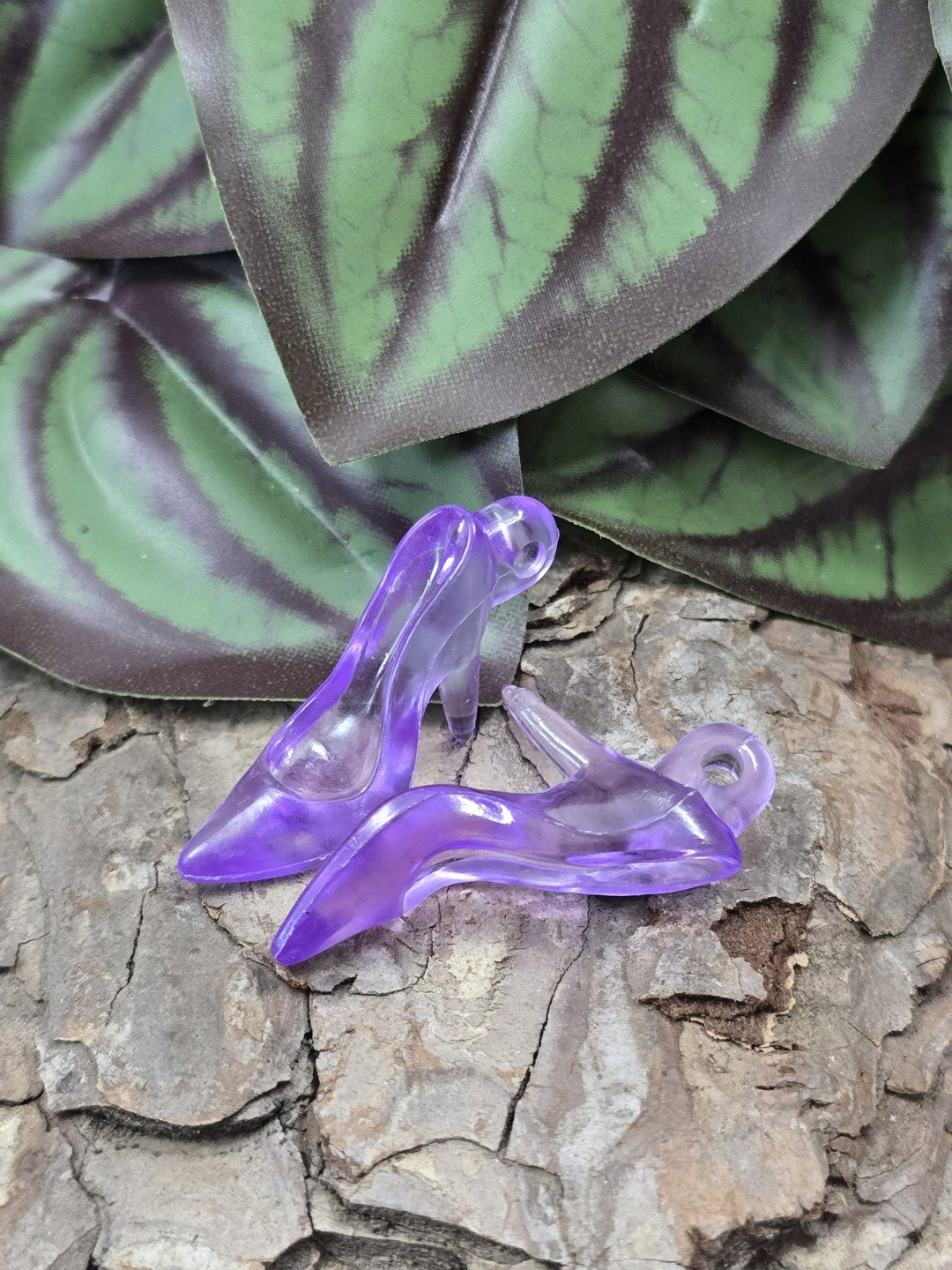 Zwei lila transparente Acryl-Pumps als Miniatur-Schuhanhänger auf Baumrinde