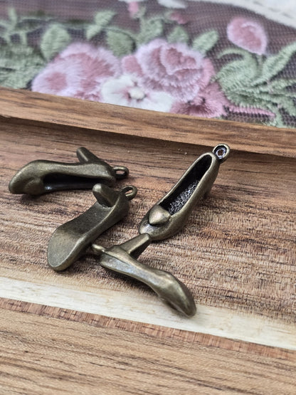 Vier Pumps-Schuh-Anhänger in Antikbronze aus verschiedenen Blickwinkeln auf Holzgrund.