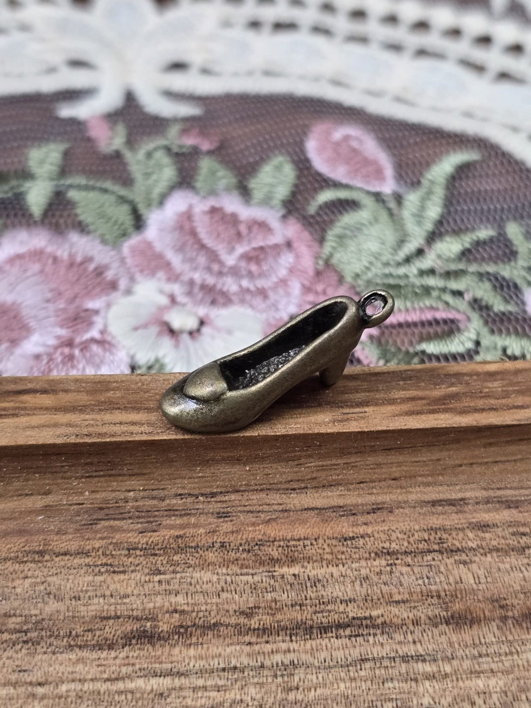 Dreidimensionaler Pumps-Anhänger in Bronze-Optik seitlich auf Holz platziert.