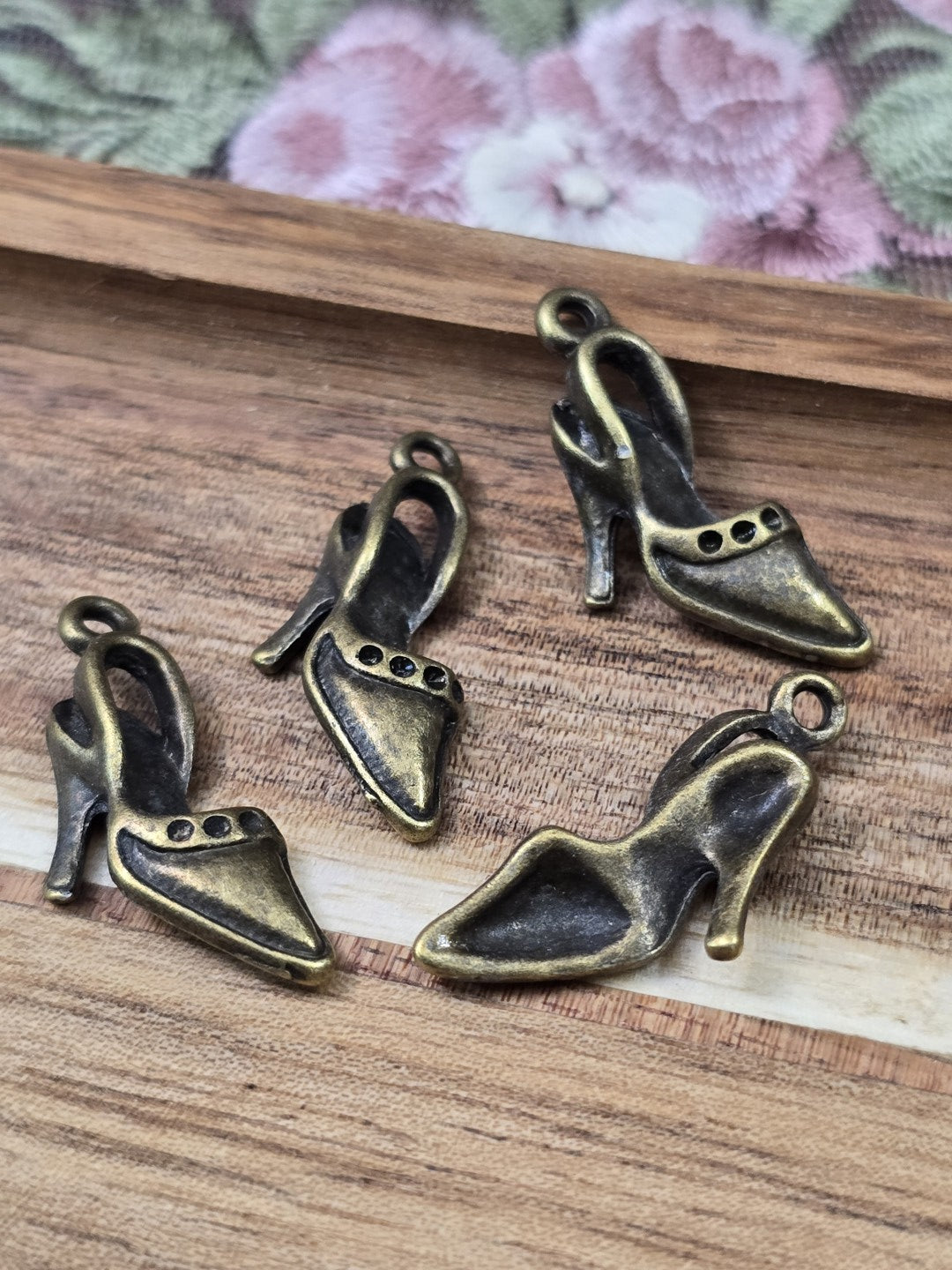 Vier elegante Pumps-Schmuckanhänger in Antikbronze mit Öse flach liegend auf Holz.