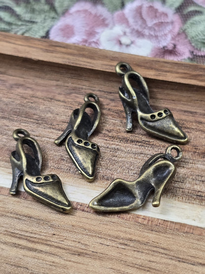 Vier elegante Pumps-Schmuckanhänger in Antikbronze mit Öse flach liegend auf Holz.