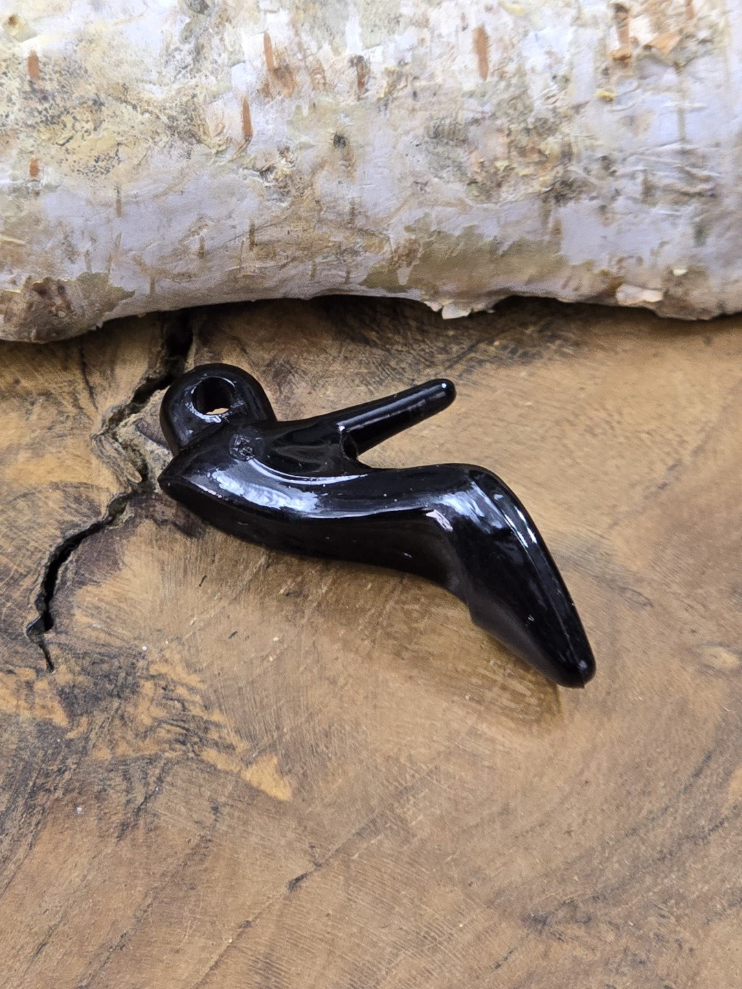Schwarzer Schuh-Charm aus Acryl mit Lochöse, liegend auf Holz fotografiert