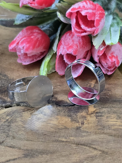 Zwei silberfarbene verstellbare Ringrohlinge mit flacher 15mm Klebeplatte vor rosa Tulpen auf Holzgrund.