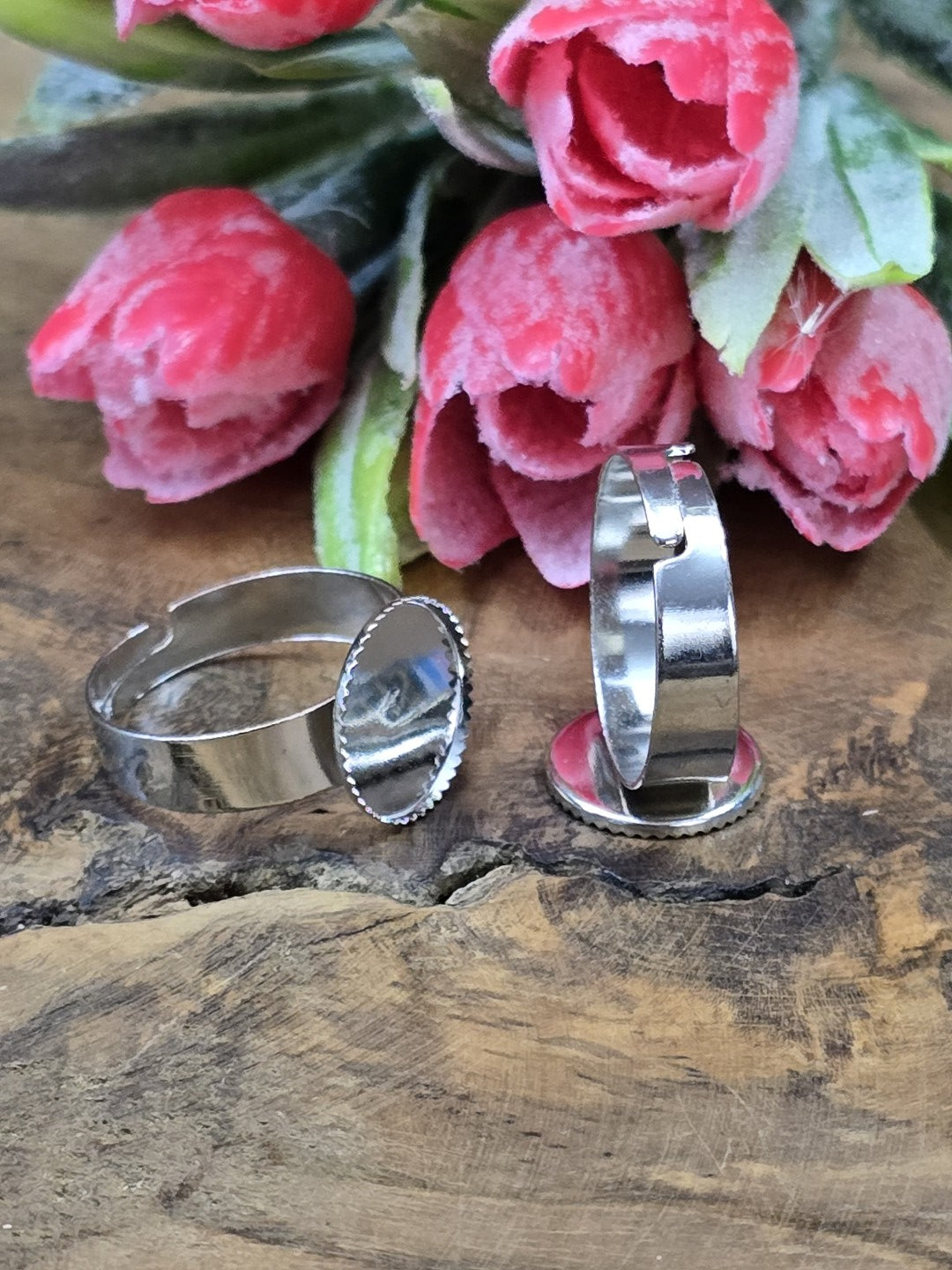 Zwei silberne verstellbare Ringrohlinge mit runder 12mm Cabochon-Fassung vor rosa Deko-Blumen auf Holzgrund.