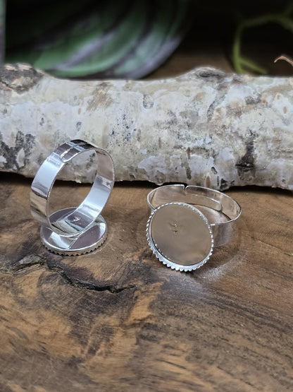 Zwei silberne Ringrohlinge mit runder 12mm Klebefläche und gezacktem Fassungsrand auf Holz vor einer Birkenrinde.