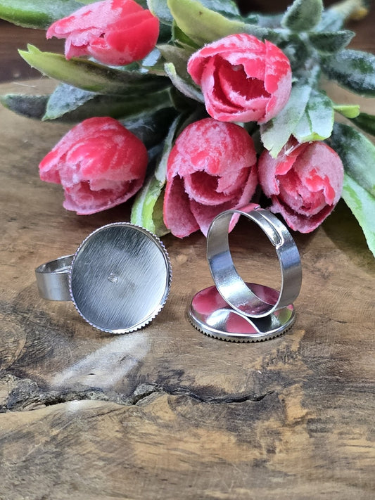 Zwei silberne verstellbare Ringrohlinge mit runder 18mm Cabochon-Fassung vor rosa Tulpen auf Holzgrund.