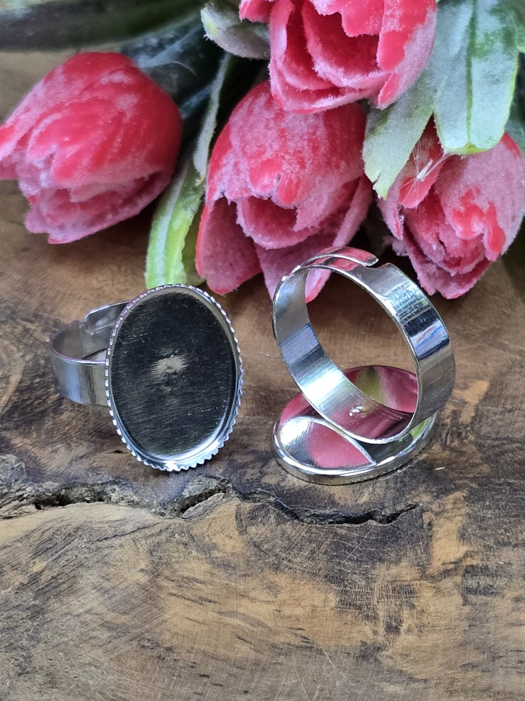 Silberne Ringrohlinge mit ovaler 18x13mm Cabochon-Fassung und gezacktem Fassungsrand vor rosa Tulpen.
