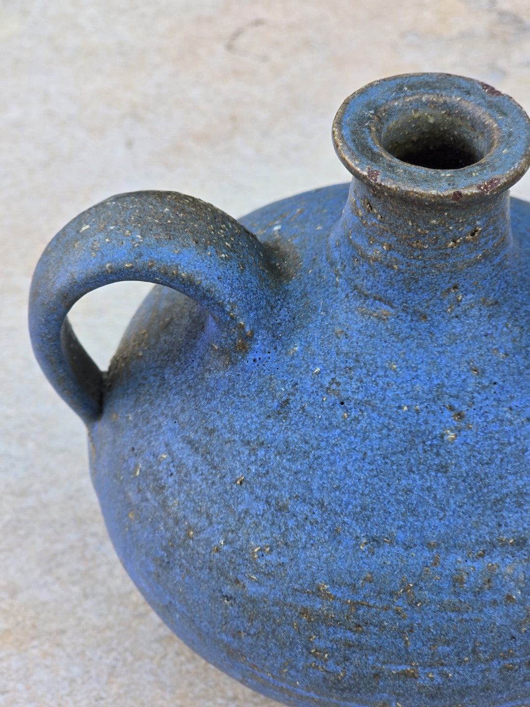 Kleine signierte Keramikvase von Rudi Stahl mit blau matter Oberfläche, bauchiger Form, seitlichem Henkel und rotbraunem unglasiertem Boden.