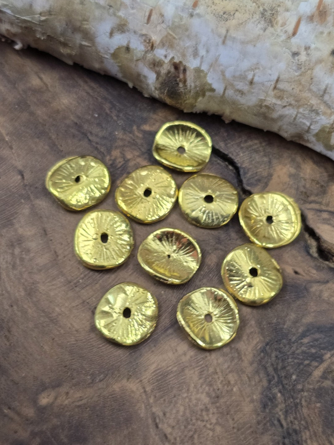 Zehn filigran gewölbte, vergoldete Scheibenperlen (10 mm) dekorativ auf einer rustikalen Holzscheibe arrangiert.
