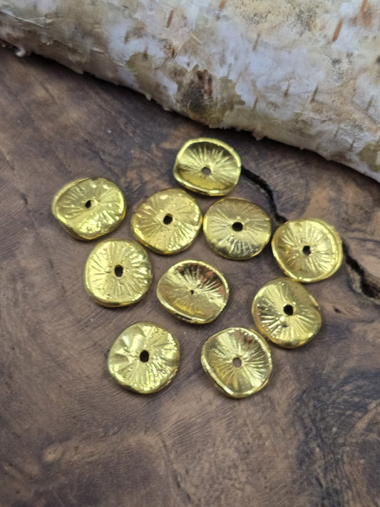 Zehn filigran gewölbte, vergoldete Scheibenperlen (10 mm) dekorativ auf einer rustikalen Holzscheibe arrangiert.