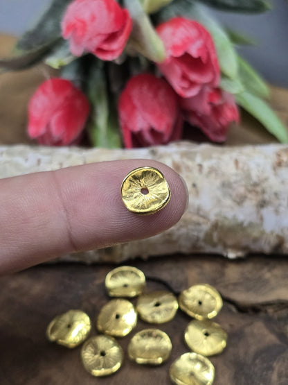 Eine winzige vergoldete Scheibenperle (10 mm) auf einer Fingerkuppe präsentiert als Größenvergleich für DIY-Schmuckzubehör.