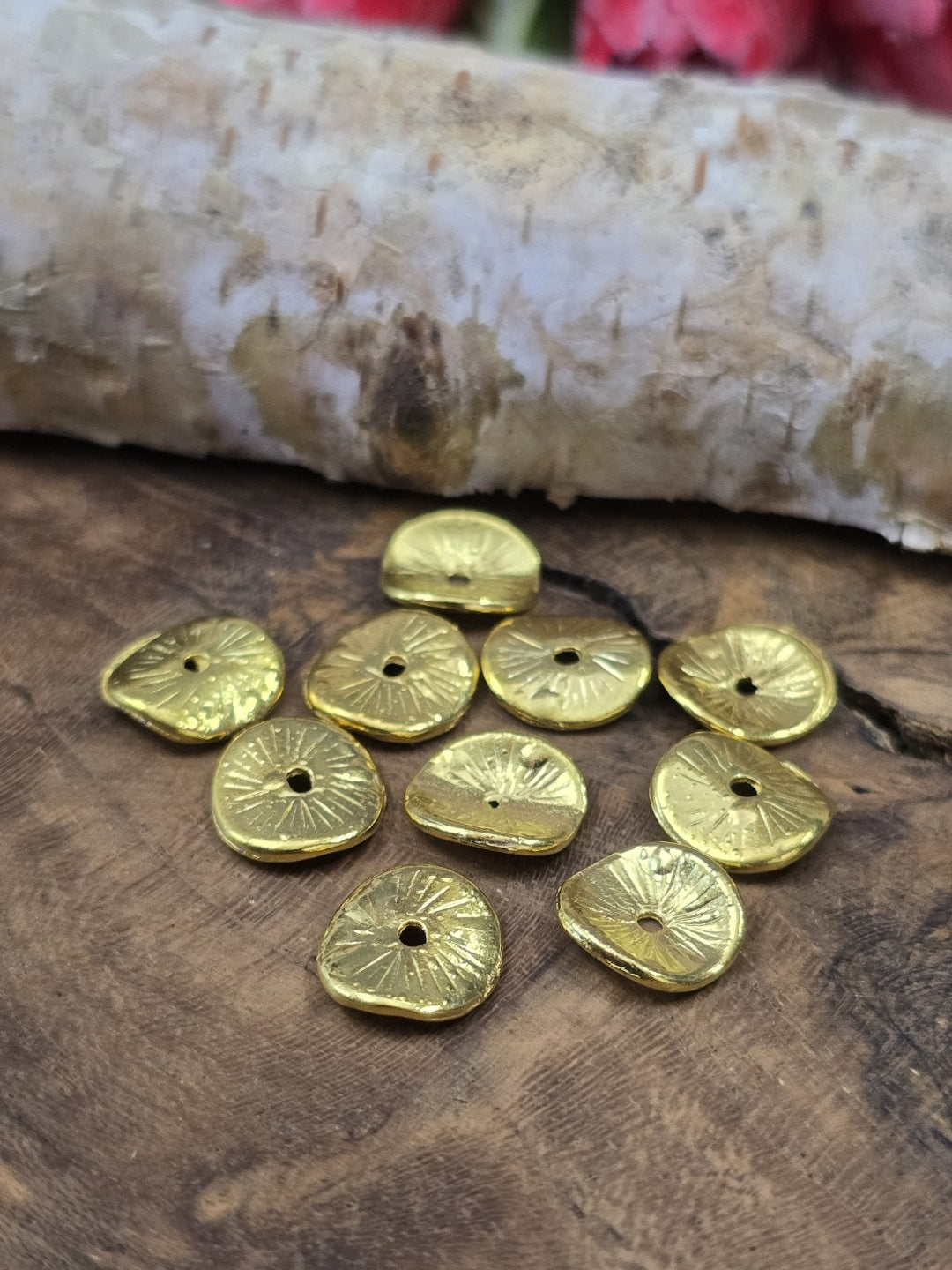 Nahaufnahme von vergoldeten, gewölbten Metallscheiben-Perlen mit feiner Struktur auf Echtholz vor Birkenrinde.