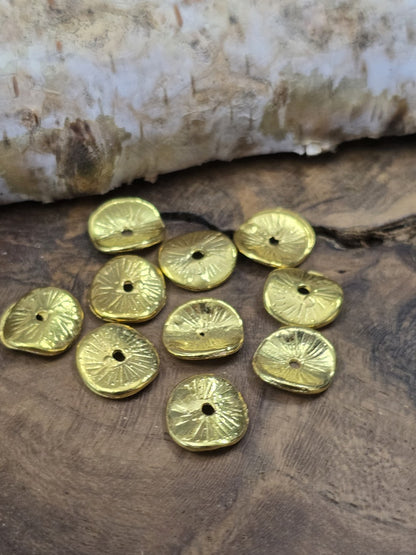 Zehn goldfarbene, nach innen gewölbte Metall-Diskusperlen (10 mm) zum Basteln von Ketten und Armbändern auf Holzgrund.