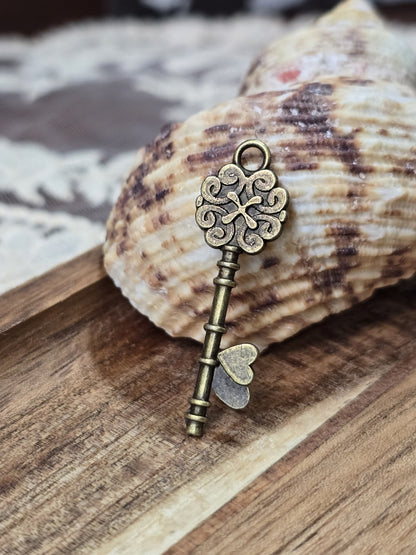 Schlüssel-Schmuckanhänger in Bronze-Optik mit Öse dekoriert vor einer Muschel auf Holz.