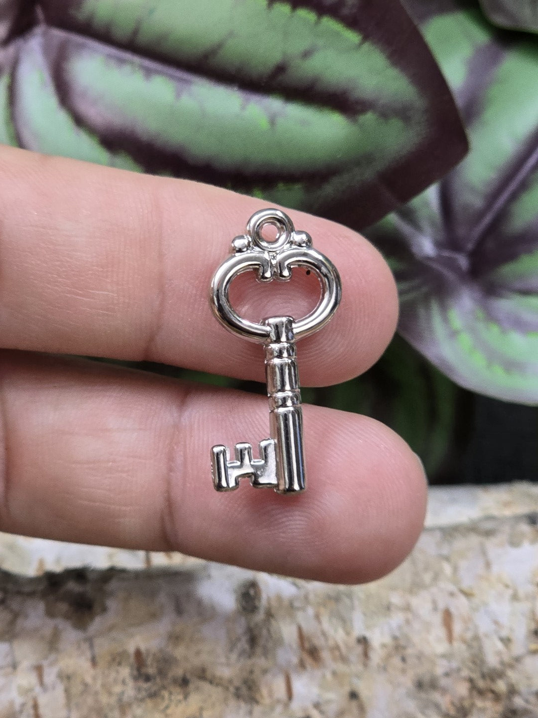 Silberner Schlüssel-Charm 26 mm als Größenvergleich zwischen zwei Fingern gehalten