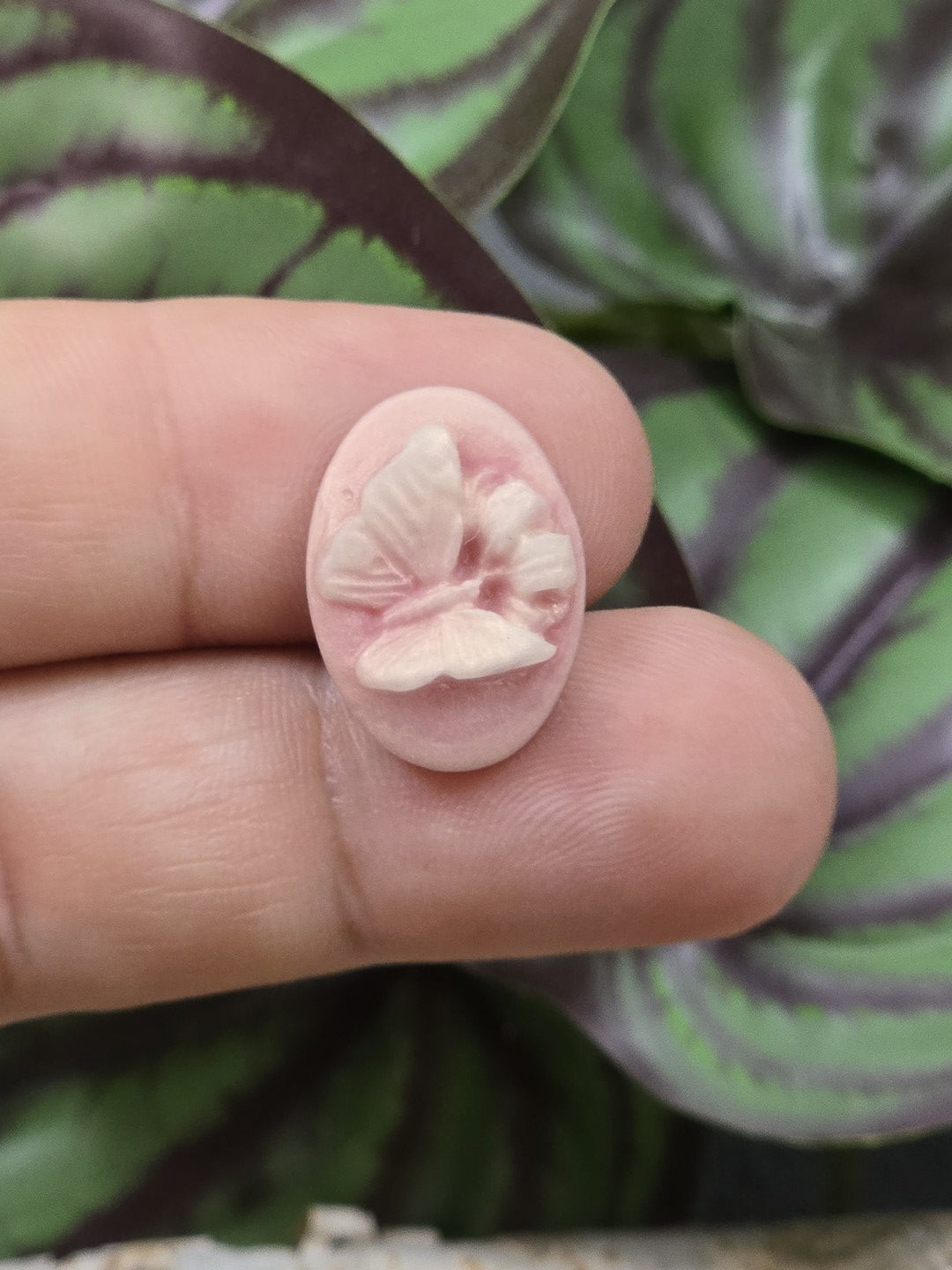 Kleiner altrosa Schmetterling Cabochon auf Fingerspitzen zur Größendarstellung