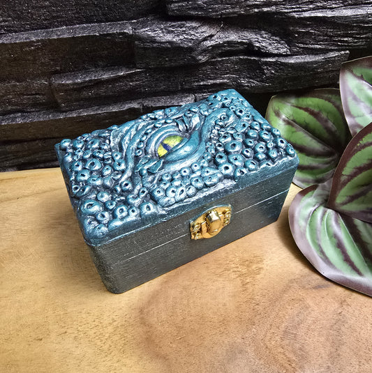 Das Bild zeigt eine geheimnisvolle Schatulle Auge des Oktopus, Meeresgrün, mit Samtkissen und Schnappverschluss. Ladetruhe, Würfelbox, Schmuckkiste

Ob als Schmuckschatulle, Ladebox, Würfelbox oder für andere Kostbarkeiten – diese einzigartige Truhe ist nicht nur ein praktisches Behältnis, sondern ein magisches Artefakt, das die Geschichten der Meere in sich trägt.
