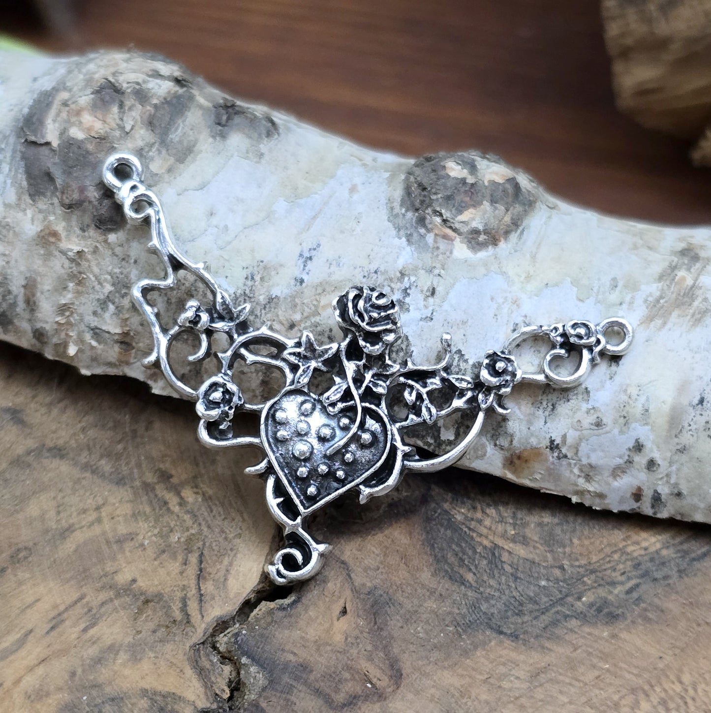 Das Bild zeigt eine Schmuckkomponente für Ketten, Choker und Armbänder. Der Verbinder ist antik silberfarbig und kann z.B. durch colorieren zu einem ganz persönlichen Schmuckteil werden. In der Mitte befindet sich ein Herz, umgeben von Rosen.