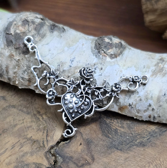 Das Bild zeigt eine Schmuckkomponente für Ketten, Choker und Armbänder. Der Verbinder ist antik silberfarbig und kann z.B. durch colorieren zu einem ganz persönlichen Schmuckteil werden. In der Mitte befindet sich ein Herz, umgeben von Rosen.
