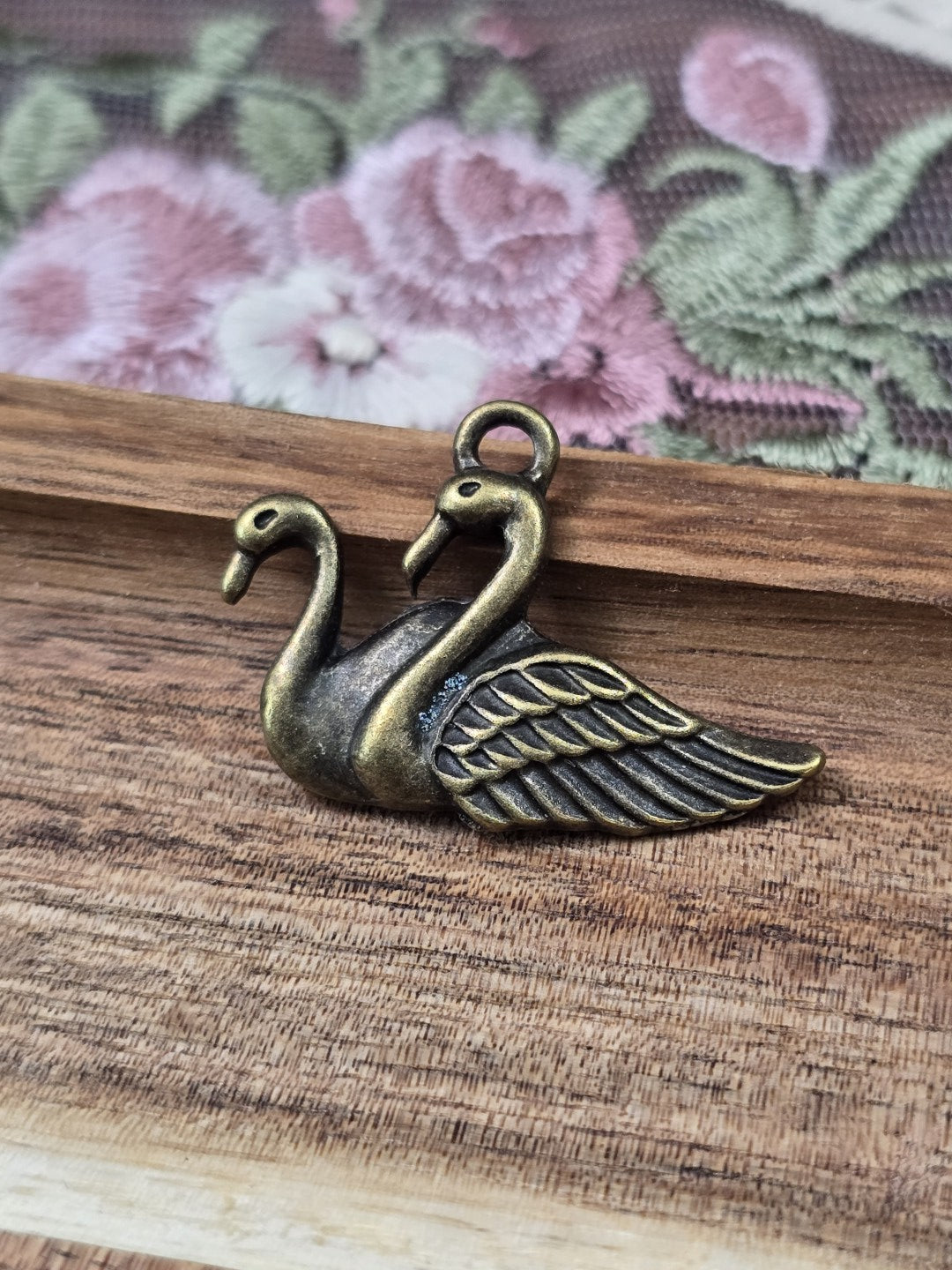 Schwan-Anhänger in Antik-Bronze für Schmuckherstellung liegend auf Holzgrund.