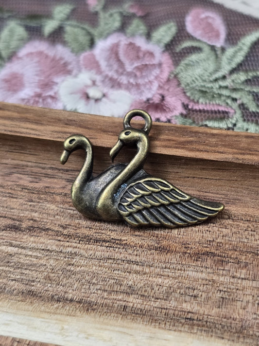 Schwan-Anhänger in Antik-Bronze für Schmuckherstellung liegend auf Holzgrund.