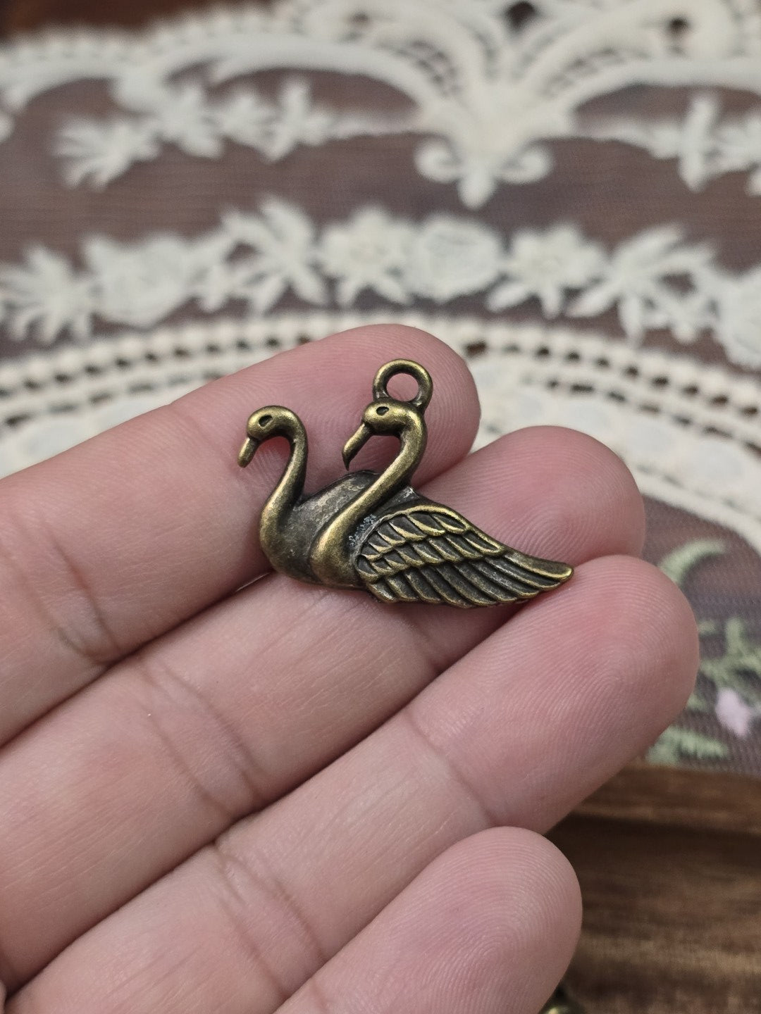 Schwanen-Schmuckanhänger 21x28mm in Bronze-Optik gehalten in der Hand als Größenvergleich.