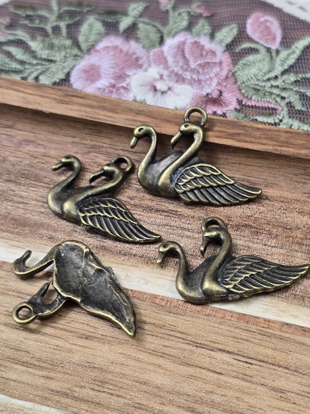 Vier Schwan-Anhänger in Antik-Bronze von Vorder- und Rückseite auf Holzbrett.