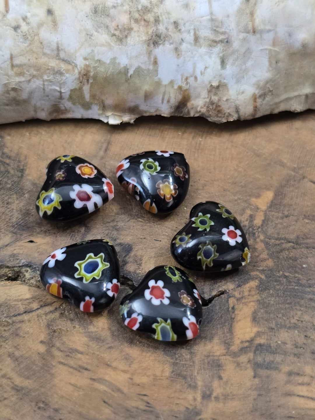 Nahaufnahme von fünf glänzenden Herz-Millefiori-Glasperlen in Schwarz mit bunten Blumenmotiven für DIY-Schmuck.