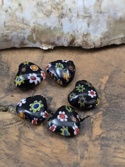 Nahaufnahme von fünf glänzenden Herz-Millefiori-Glasperlen in Schwarz mit bunten Blumenmotiven für DIY-Schmuck.