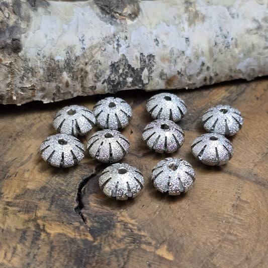 10 silberfarbene Stardust-Metallperlen, 10 x 6 mm, in UFO-Form mit glitzernder Oberfläche und gefächertem Rand. Ideal für Schmuckprojekte wie Armbänder, Ketten oder Ohrringe. Fädelloch: 1,6 mm. Perfekt für edle und stilvolle Akzente.