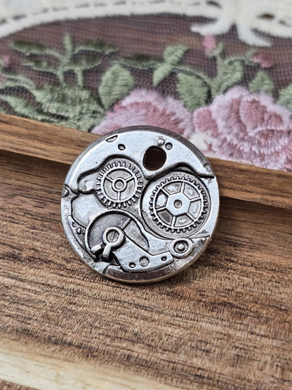 Runder Steampunk Anhänger in Antik-Silber mit Zahnrädern und Uhrwerk-Motiv auf Holzuntergrund.
