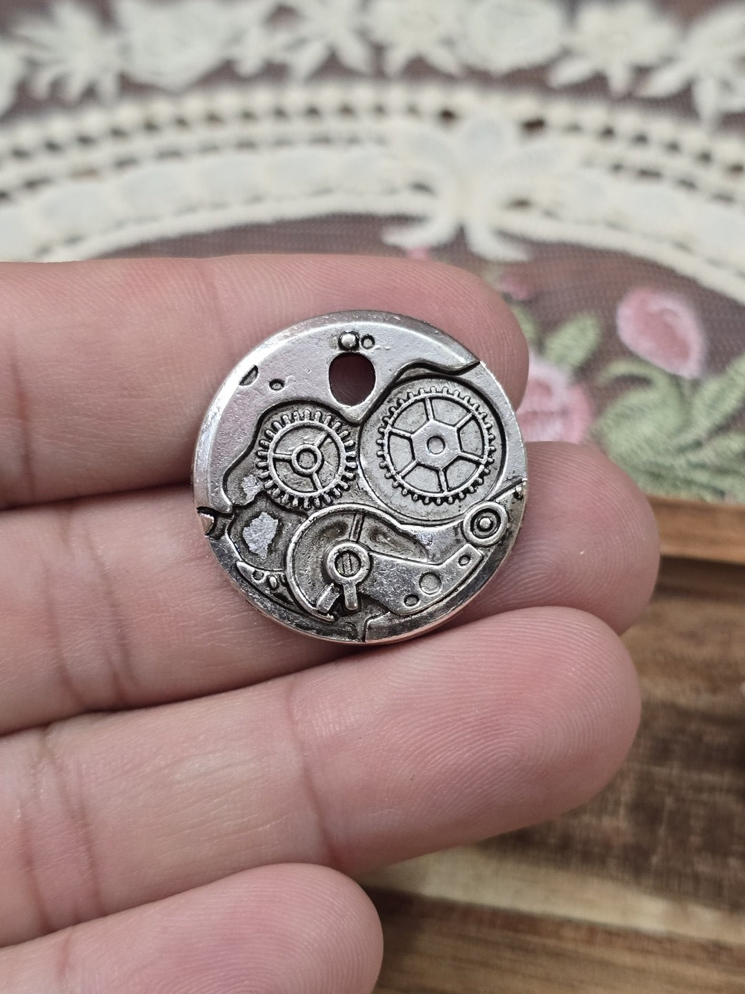 Runder Schmuckanhänger 25mm mit Zahnrad-Muster in Antik-Silber gehalten zwischen zwei Fingern.