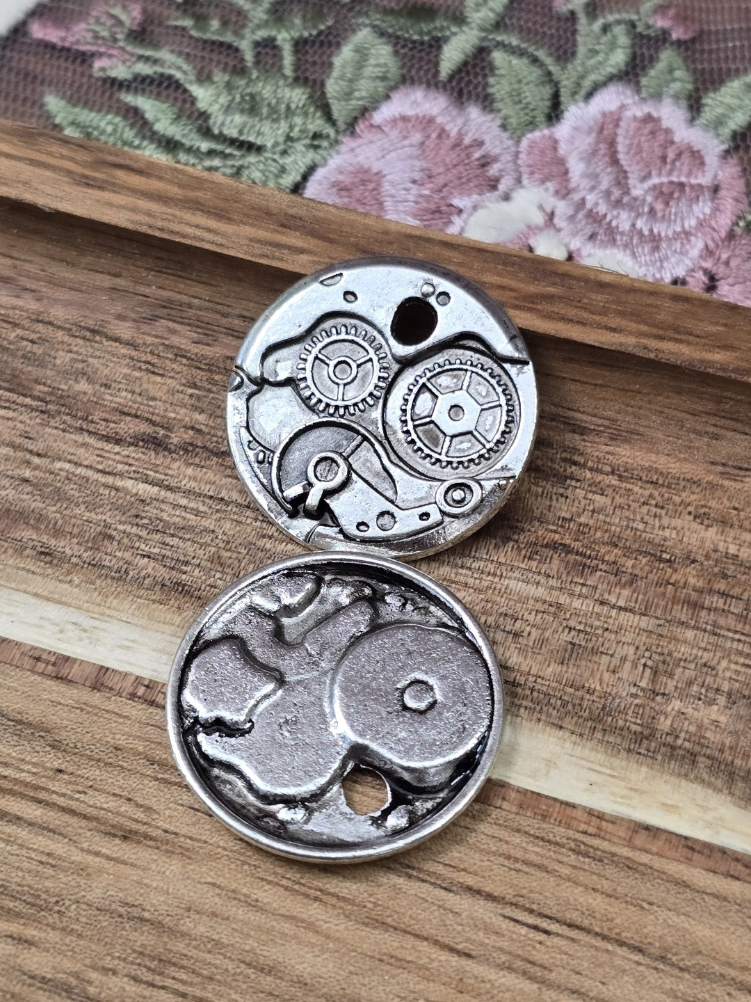Vorderseite und Rückseite des runden Steampunk Metallanhängers mit Zahnrädern auf Holz.