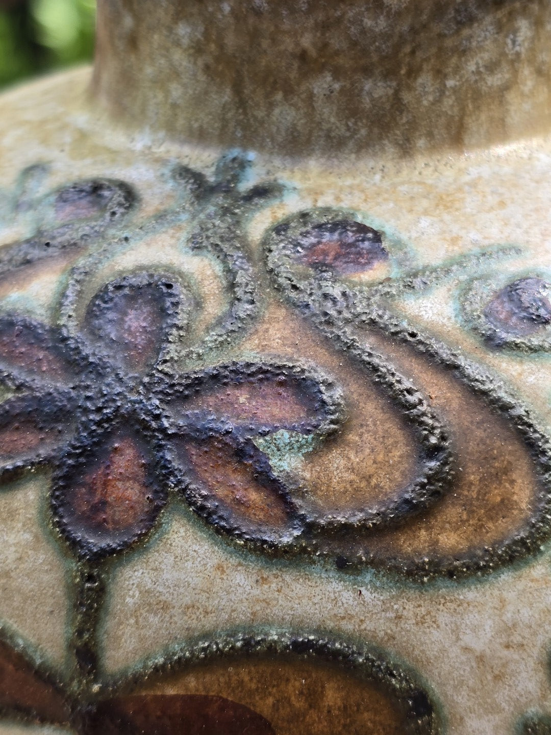 Nahaufnahme des floralen Reliefdekors mit braunen Blättern, grünen Konturen und rauer Struktur