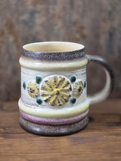 Vintage Keramikbecher von Strehla mit hellem Korpus, gelbem Blütenrelief, grünen Punkten und dunklem Henkel in Frontalansicht