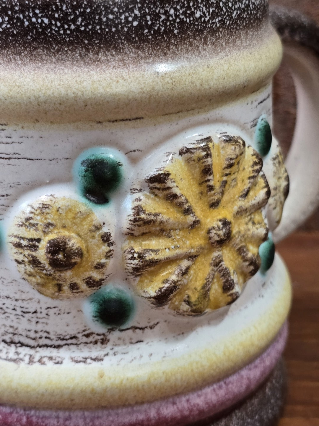 Vintage Keramikbecher mit floralem Reliefdekor in Gelb und Braun sowie grünen Punkten auf heller Oberfläche in Nahaufnahme