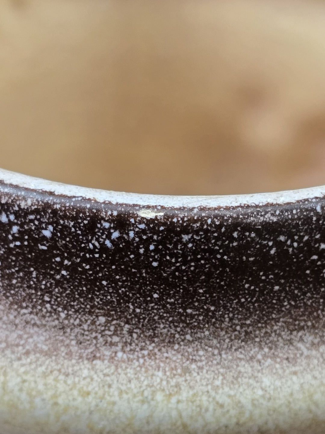 Vintage Keramikbecher mit dunkel gesprenkeltem oberen Rand und kleiner sichtbarer Abplatzung an der Kante in Detailaufnahme