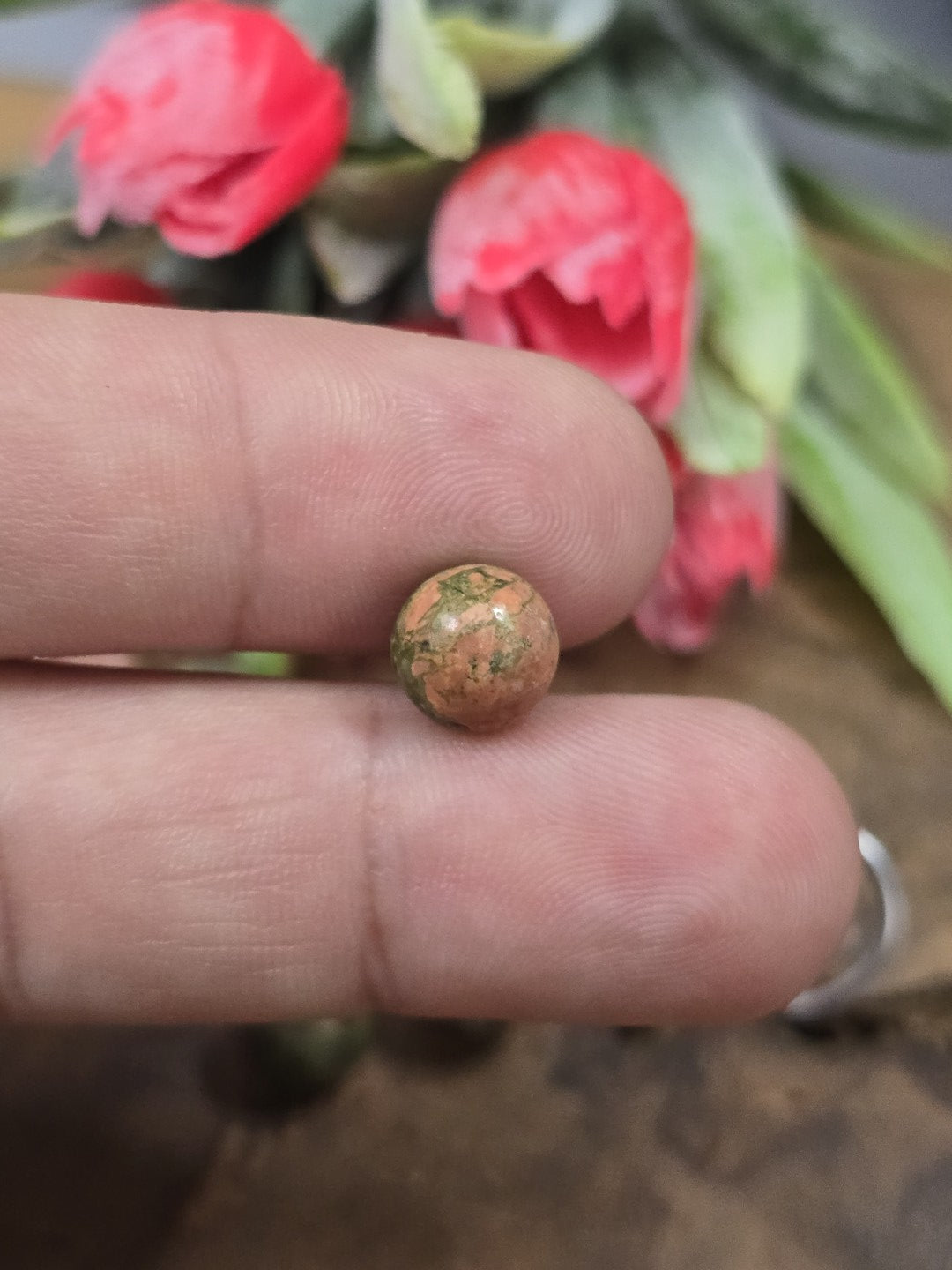 Eine 8 mm Unakit-Perle zwischen zwei Fingerkuppen gehalten als Größenvergleich für DIY-Schmuckprojekte.
