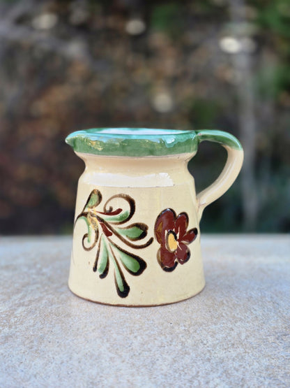 Kleine Vintage-Kanne aus vermutlich ungarischer Majolika mit cremefarbener Glasur, grünem Rand, handgemalter Blume und rotscherbigem Boden.